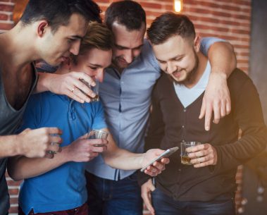 Cheerful Old Friends Communicate With Each Other And Phone Watch, Glasses Of Whiskey In Pub